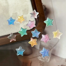 A set of small glittery star-shaped embellishments in pastel rainbow colors, scattered on a reflective surface near a wooden frame, Obroi
