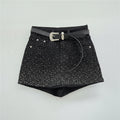 Black denim shorts embellished with silver rhinestones, featuring a black leather belt with a silver buckle, laid flat on a light gray background, Obroi