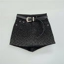Black denim shorts embellished with silver rhinestones, featuring a black leather belt with a silver buckle, laid flat on a light gray background, Obroi