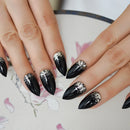 Black stiletto nails with silver glitter accents on a floral background, Obroi