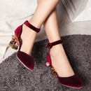 Red velvet high-heeled shoes with gold accents worn by a person on a gray carpet, Obroi