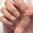 Close-up of a hand with decorative nails featuring gold accents on a light background, Obroi