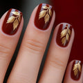 Nails with red nail polish and gold leaf designs on a dark background, Obroi