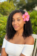 Woman with curly hair and a pink flower in her hair, standing outdoors, Obroi