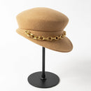 Beige hat with a gold chain on a black stand against a white background, Obroi