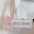 Decorative sign with a pink teddy bear illustration and 'Sweet Home' text, hanging against a neutral background, Obroi