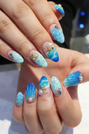Close-up of a hand with blue and white nail art featuring sea-themed decorations, Obroi