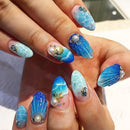Close-up of a hand with blue and white nail art featuring sea-themed decorations, Obroi