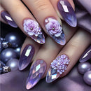 Nails with purple floral and diamond design on a purple fabric background