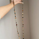 Long beaded necklace held by a hand against a neutral background, Obroi