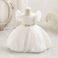 White children's dress on a mannequin against a decorative wall, Obroi