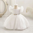 White children's dress on a mannequin against a decorative wall, Obroi