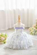 A toddler girl's floral print party dress displayed on a dress form mannequin. The dress features a white base with a light purple and green floral pattern, a lavender purple waistband with a bow, and a tiered ruffled tulle skirt, Obroi