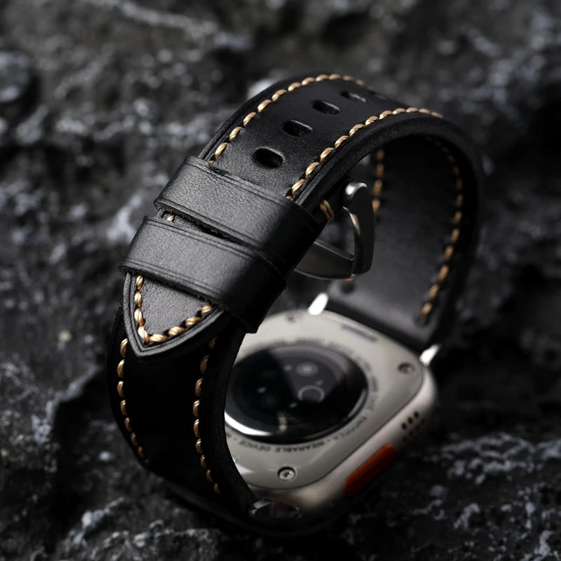 Obroi Black leather watch strap with gold stitching on a dark textured background