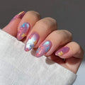 A close-up of a hand with manicured nails decorated in a pastel pink and lavender glitter base, featuring small blue and yellow flower motifs, Obroi