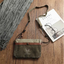 Green canvas bag with brown accent on a wooden surface next to a magazine and glasses, Obroi