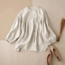 White blouse with puff sleeves on a beige surface with pink shoes and dried plants, Obroi