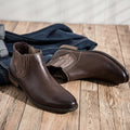 Pair of brown leather boots on a wooden floor with jeans in the background ,Obroi
