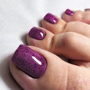 Close-up of toes with purple glitter nail polish on a white background, Obroi