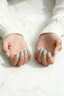 Close-up of hands with light blue nail polish on a white background, Obroi