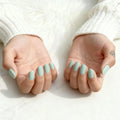 Close-up of hands with light blue nail polish on a white background, Obroi