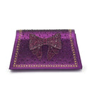 A purple rhinestone-embellished clutch bag with a matching bow on the front and a border of gold rhinestones, shown on a plain white background, Obroi