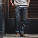 Person wearing dark blue jeans and brown boots standing against a textured wall.