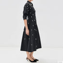 A model wearing a black midi dress with white embroidered details, shown from a side profile against a plain white studio background, Obroi