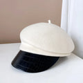 White beret with a black crocodile-patterned visor on a white surface, Obroi