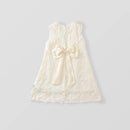 An ivory sleeveless lace dress for toddlers, featuring a large satin bow at the center front, scalloped lace trim, and embroidered floral details, shown against a light gray background, Obroi