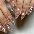 Close-up of manicured fingernails with a glossy nude-pink base, gold metallic swirl and crescent designs, pearl accents, and glitter details, Obroi