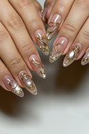 Close-up of manicured fingernails with a glossy nude-pink base, gold metallic swirl and crescent designs, pearl accents, and glitter details, Obroi