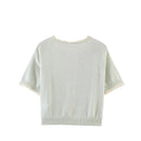 A pale sage green knit short-sleeve top with delicate lace trim at the collar and sleeve cuffs, shown from the back on a white background with the brand name Zeralns in the top left corner, Obroi