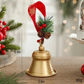 A small gold Christmas bell ornament with a red hanging ribbon, green pine sprigs, and pinecones, shown on a tabletop with dimension labels reading 10cm, 8cm, and 80g, Obroi