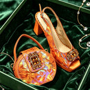 A pair of metallic orange slingback high-heeled shoes and a matching small handbag with jeweled embellishments, displayed inside a green velvet box with a chain necklace nearby, Obroi