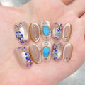 Nails with floral and blue accent designs on a hand, Obroi