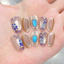 Nails with floral and blue accent designs on a hand, Obroi
