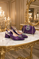 A pair of sparkling purple slingback heels with jeweled embellishments and a matching purple quilted handbag with a chain strap, displayed on a marble and gold console table in an ornate room, Obroi