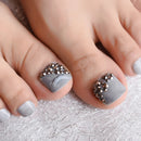 Close-up of toes with gray nail polish and decorative elements on a textured surface, Obroi