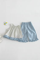 A baby girl's two-piece clothing set laid flat on a textured white background. The set includes a sleeveless top in cream and light blue with vertical stripes and a ruffled hem, paired with light blue elastic-waist shorts, Obroi