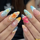Close-up of hands displaying a set of long almond-shaped nails with intricate Japanese-inspired nail art designs, including floral patterns, 3D flower embellishments, and shell motifs, Obroi