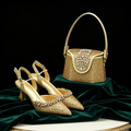 A pair of gold pointed-toe high heels with crystal embellishments is displayed next to a matching gold handbag with a crystal-embellished flap, set on draped dark green velvet against a black background, Obroi