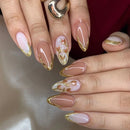 Obroi Close-up of hands with pink and gold nail design on a neutral background
