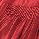 Close-up of a red pleated fabric garment, showing the texture and folds of the material, Obroi