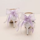 White high-heeled shoes with purple ribbons and butterfly decorations on a light background, Obroi