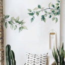 Decorative wall with green leafy branches, a patterned pillow, and plants, Obroi
