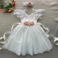 White lace dress with pink floral sash on a gray surface, Obroi