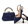 Navy blue glittery handbag and high-heeled shoes with decorative elements on a white background, Obroi