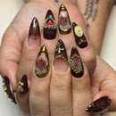 Obroi Hand with dark brown nail art featuring gold accents and decorative elements.
