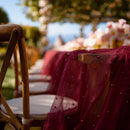 Maroon draped fabric over wooden chairs with blurred outdoor setting, Obroi